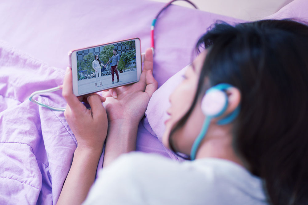 Image of Girl in Bed Streaming Video On Mobile Phone
