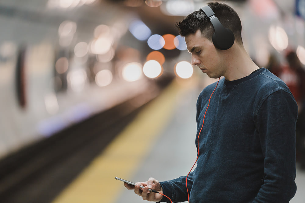 Millennial listens to podcast with headphones on smartphone in subway