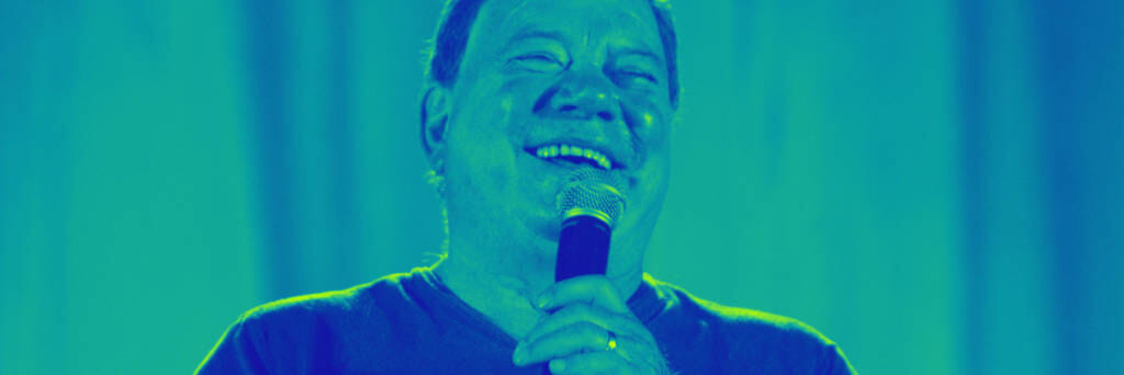william shatner laughing and holding microphone
