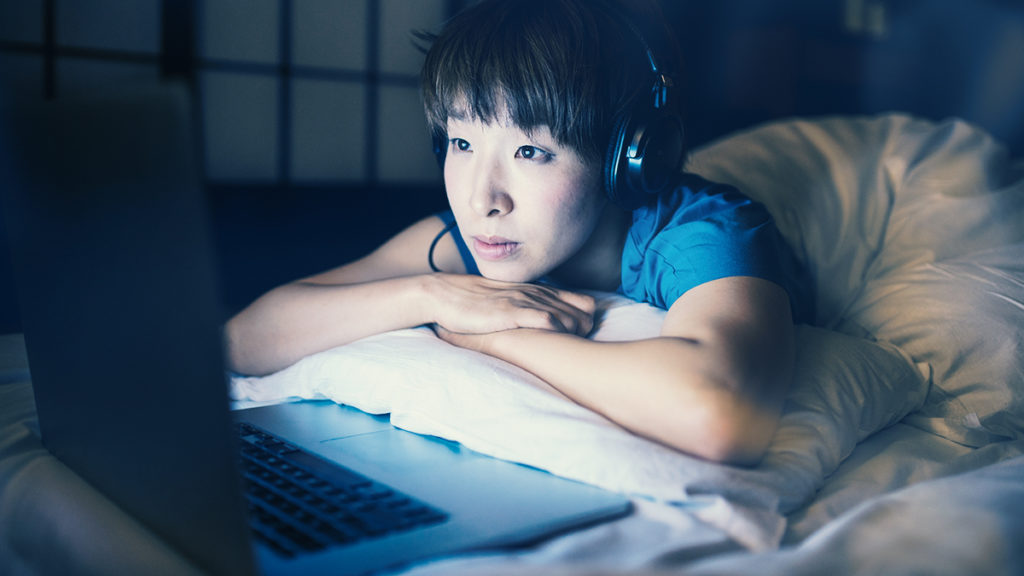 Woman watching tv from laptop while laying in bed